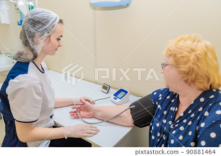 A nurse in a polyclinic measures the blood pressure of a woman with a device. Healthcare 90881464