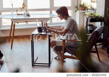 Smiling Asian guy in headphones working with laptop at home while typing 90883440
