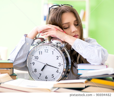 Young female student preparing for exams with many books in time 90894482