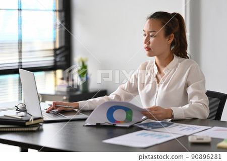 Focused young female business entrepreneur sitting at her personal office and using laptop computer 90896281