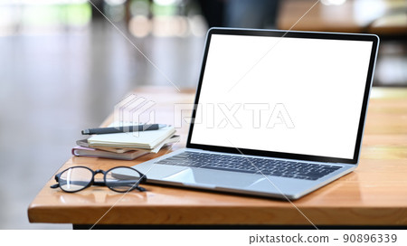 Computer laptop with white empty display, eyeglasses and notebooks on wooden office desk 90896339