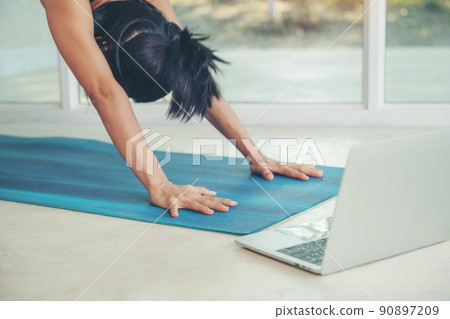.Woman do yoga downward facing dog pose inside light cozy room through window seen green foliage trees summer.stretching watching fitness video tutorial online on laptop, doing workout at home sitting .Woman do yoga downward facing dog pose inside light cozy room through window seen green foliage trees summer.stretching watching fitness video tutorial online on laptop, doing workout at home sitting 90897209