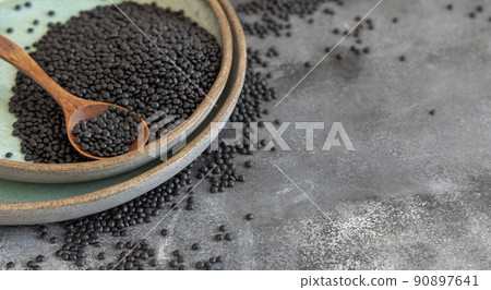 Plate of dry black lentils beans with a spoon on grey table close up, protein source for vegetarian diet 90897641