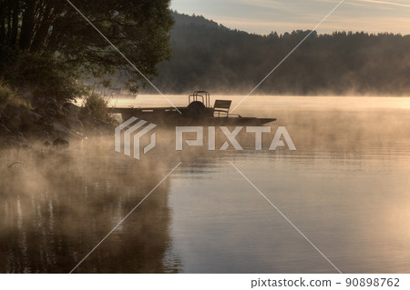 Sunrise over the lake in fog, pier and pedal boat, summer morning, Predni Vyton, Lipno lake, Czech republic 90898762