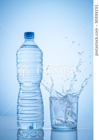 Mineral water bottle and water glass with spash on blue background with copy space. Vertical format. Mineral water bottle and water glass with spash on blue background with copy space. Vertical format. 90899291