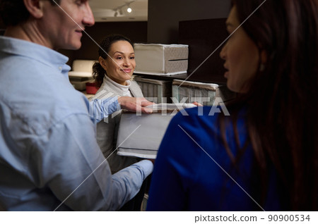 A married couple in a furniture store inspects the orthopedic mattress sample before buying, standing near a pleasant experienced sales consultant A married couple in a furniture store inspects the orthopedic mattress sample before buying, standing near a pleasant experienced sales consultant 90900534