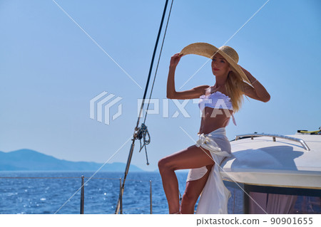 Beautiful young blond woman in bikini standing on catamaran at sunny summer day Beautiful young blond woman in bikini standing on catamaran at sunny summer day 90901655