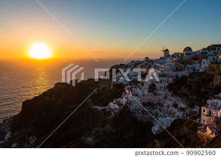 Sunset, white cityscape and windmill seen from Oia Castle in Oia, Santorini, Greece. 90902560