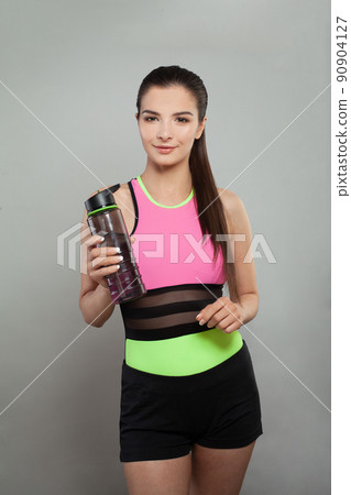 Smiling active woman holding water bottle or protein shake on grey background 90904127