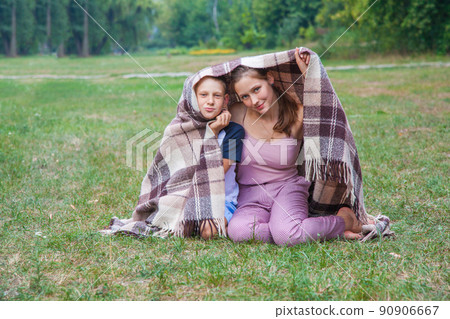 Young sister and brother with freckles on their faces stand covered with plaid in park, get warm, smiling and looking at camera. Young sister and brother with freckles on their faces stand covered with plaid in park, get warm, smiling and looking at camera. 90906667