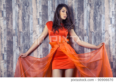 Young brunette woman in stylish orange silk dress posing on wooden background Young brunette woman in stylish orange silk dress posing on wooden background 90906670