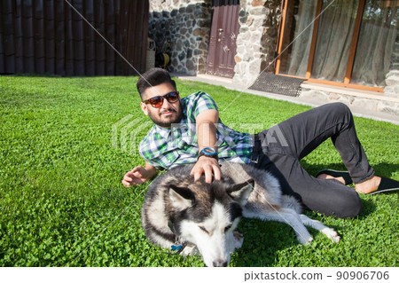 Young man sitting at green lawn and enjoying with his dog Young man sitting at green lawn and enjoying with his dog 90906706