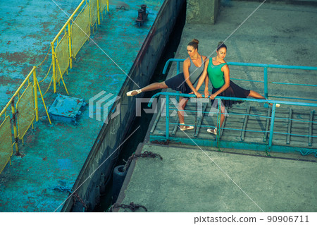 Two young beautiful twin sister dancing ballet in the city with ballet costume. urban sync dance. industrial street dancing. with special effect. synced posing. pointe ballet shoes and dress. 90906711
