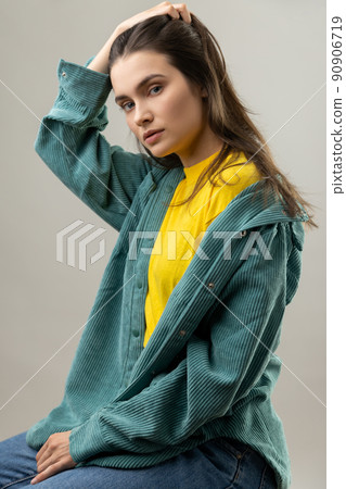 Portrait of attractive beautiful woman sitting with hand in head, looking at camera with pensive expression, wearing casual style jacket. Indoor studio shot isolated on gray background. Portrait of attractive beautiful woman sitting with hand in head, looking at camera with pensive expression, wearing casual style jacket. Indoor studio shot isolated on gray background. 90906719