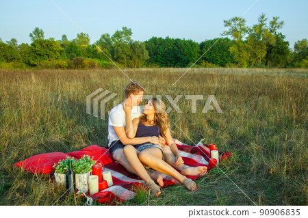 Beautiful young happy loving couple on picnic lying down on plaid on sunny summer day enjoying and resting. hugging and looking at each other and smiling. Beautiful young happy loving couple on picnic lying down on plaid on sunny summer day enjoying and resting. hugging and looking at each other and smiling. 90906835