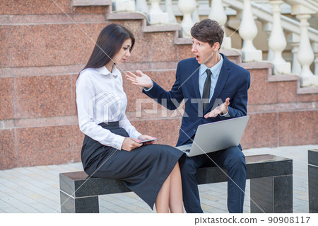 Boss in blue suit and his assistant in white blouse and black skirt discussing their work outdoors. 90908117