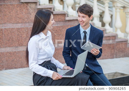 Boss in blue suit and his assistant in white blouse and black skirt discussing their work outdoors. 90908265