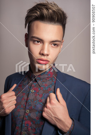 Handsome young fashion model with highlighted undercut haircut posing in blue suit in studio looking with passion and holding his suit. Handsome young fashion model with highlighted undercut haircut posing in blue suit in studio looking with passion and holding his suit. 90908507
