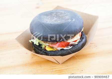 black burger with beef stew and cheese with tomato and salad leaf served on paper box over wooden surface 90909467