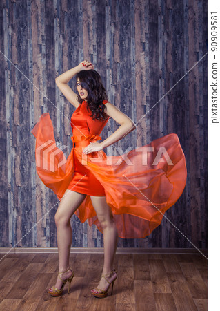 Young brunette woman in stylish orange silk dress posing on wooden background Young brunette woman in stylish orange silk dress posing on wooden background 90909581