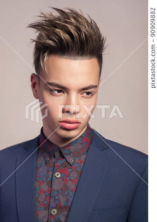 Handsome young fashion model with highlighted undercut haircut posing in blue suit in studio looking sad. 90909882