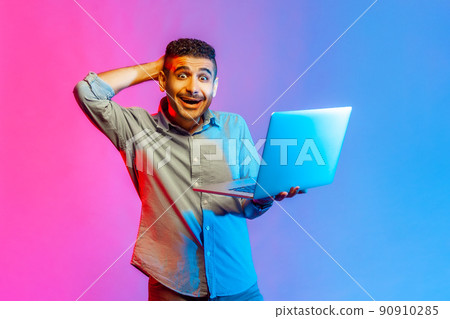 Portrait of man in shirt looking at camera with amazed expression, watching shocking content, surprised by news, raised arm. Indoor studio shot isolated on colorful neon light background. Portrait of man in shirt looking at camera with amazed expression, watching shocking content, surprised by news, raised arm. Indoor studio shot isolated on colorful neon light background. 90910285