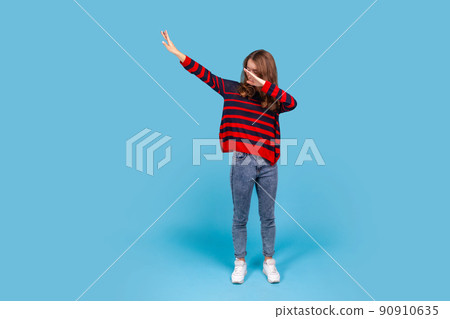 Full length portrait of woman wearing striped casual style sweater, hiding face with dab dance move, performing internet meme of success, dabbing trends. Indoor studio shot isolated on blue background Full length portrait of woman wearing striped casual style sweater, hiding face with dab dance move, performing internet meme of success, dabbing trends. Indoor studio shot isolated on blue background 90910635