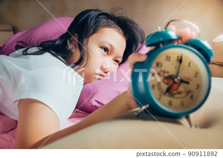 Unhappy girl waking up in bed with alarm clock. Young girl in the morning. Students wake up early to go to school. Unhappy girl waking up in bed with alarm clock. Young girl in the morning. Students wake up early to go to school. 90911892