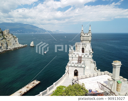 Castle Swallow's Nest on the rock over the Black Sea close-up, Crimea. It is a tourist attraction of Crimea. Amazing aerial view of the Crimea coast with the castle above abyss on sunny day. 90913027