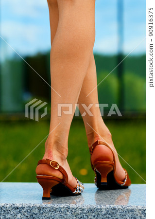 Closeup back view of slender female legs in sandals on pavement 90916375