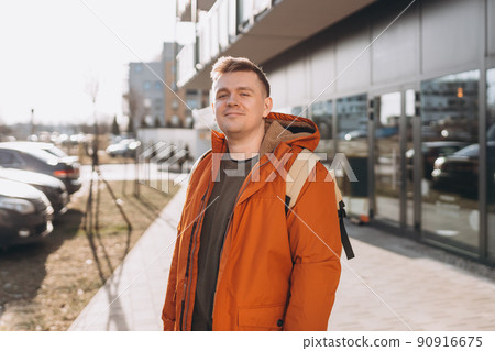 A handsome young man with backpack walking on the street in the city. Urban lifestyle concept. Traveler. Spring time. Portrait of happy young man in casual clothing looking at camera outdoor. A handsome young man with backpack walking on the street in the city. Urban lifestyle concept. Traveler. Spring time. Portrait of happy young man in casual clothing looking at camera outdoor. 90916675