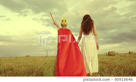 happy family. boy son with mother plays red cape superhero meadow. happy family concept. chidhood dream. golden crown on his head. child dream kid protect help group people. teamwork. fantastic game. 90918646
