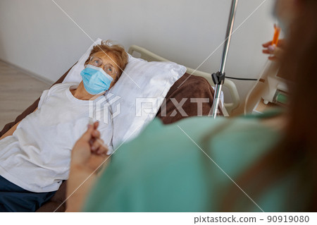 Nurse putting a drip in the arm of her patient in mask in modern medical clinic Nurse putting a drip in the arm of her patient in mask in modern medical clinic 90919080