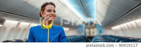 Joyful flight attendant standing in aircraft passenger cabin Joyful flight attendant standing in aircraft passenger cabin 90919117