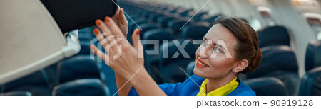 Air hostess putting travel bag in overhead luggage bin in airplane Air hostess putting travel bag in overhead luggage bin in airplane 90919128
