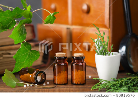 Bottles of homeopathy granules, cabinet with homeopathic remedies and old books on background. Homeopathy medicine concept. Bottles of homeopathy granules, cabinet with homeopathic remedies and old books on background. Homeopathy medicine concept. 90919570