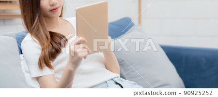 Young attractive asian woman resting using browsing tablet computer on sofa at home. 90925252