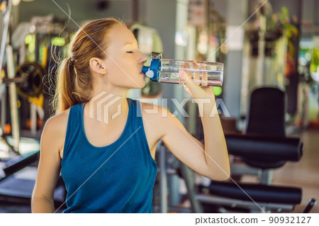 Young athletic woman drinking water in gym Young athletic woman drinking water in gym 90932127