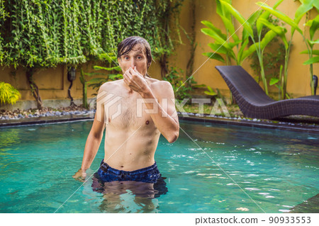 Young man with disgust on his face pinches nose, something stinks, very bad smell in swimming pool because of pool chemicals. Negative emotion facial expression 90933553