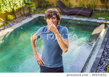 Young man with disgust on his face pinches nose, something stinks, very bad smell in swimming pool because of pool chemicals. Negative emotion facial expression 90933650