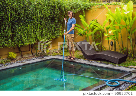 Cleaner of the swimming pool . Man in a blue shirt with cleaning equipment for swimming pools. Pool cleaning services Cleaner of the swimming pool . Man in a blue shirt with cleaning equipment for swimming pools. Pool cleaning services 90933701