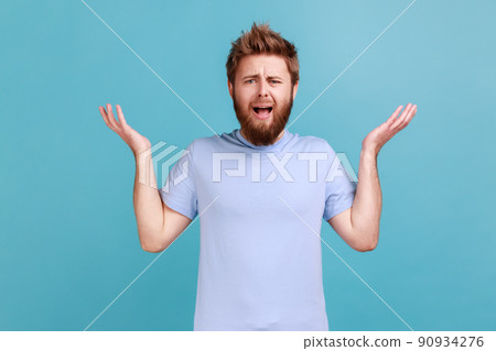 What do you want. Portrait of annoyed frustrated bearded man standing with raised hands and indignant face asking why, annoyed by problem. Indoor studio shot isolated on blue background. 90934276