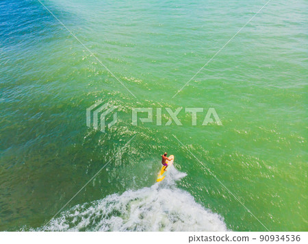 An aerial view of surfers waiting for a wave in the ocean on a clear day An aerial view of surfers waiting for a wave in the ocean on a clear day 90934536