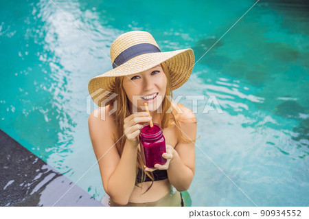 Young woman drinking Dragon fruit smoothies on the background of the pool. Fruit smoothie - healthy eating concept. Close up of detox smoothie with Dragon fruit Young woman drinking Dragon fruit smoothies on the background of the pool. Fruit smoothie - healthy eating concept. Close up of detox smoothie with Dragon fruit 90934552