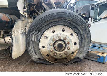 Closeup of wrecked truck wheel with a punctured or flat tire at a car junkyard after a traffic accident Closeup of wrecked truck wheel with a punctured or flat tire at a car junkyard after a traffic accident 90934556