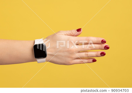 Closeup side view of woman hand with red manicure and smartwatch with empty screen and white strap, technology device. Indoor studio shot isolated on yellow background. 90934703