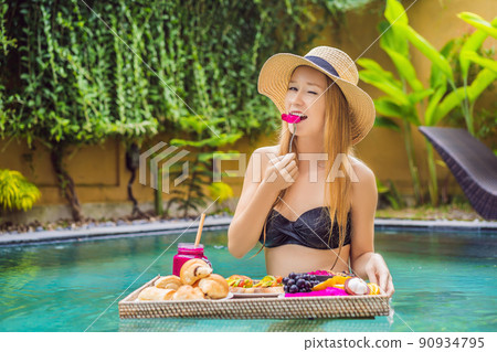 Breakfast tray in swimming pool, floating breakfast in luxury hotel. Girl relaxing in the pool drinking smoothies and eating fruit plate, smoothie bowl by the hotel pool. Exotic summer diet. Tropical Breakfast tray in swimming pool, floating breakfast in luxury hotel. Girl relaxing in the pool drinking smoothies and eating fruit plate, smoothie bowl by the hotel pool. Exotic summer diet. Tropical 90934795