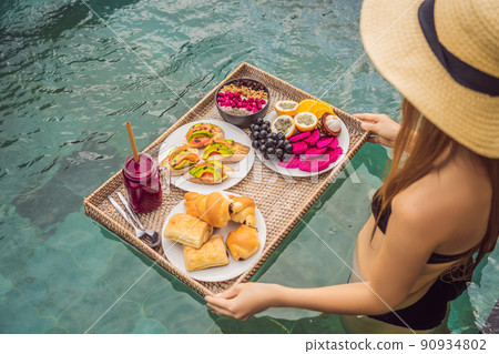 Breakfast tray in swimming pool, floating breakfast in luxury hotel. Girl relaxing in the pool drinking smoothies and eating fruit plate, smoothie bowl by the hotel pool. Exotic summer diet. Tropical Breakfast tray in swimming pool, floating breakfast in luxury hotel. Girl relaxing in the pool drinking smoothies and eating fruit plate, smoothie bowl by the hotel pool. Exotic summer diet. Tropical 90934802
