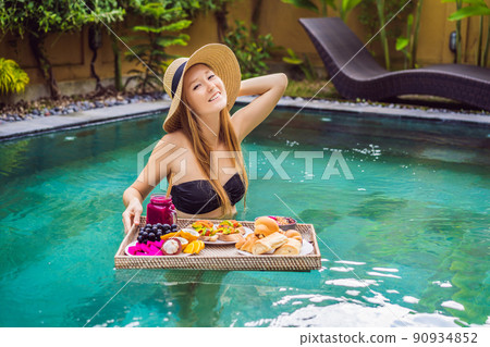 Breakfast tray in swimming pool, floating breakfast in luxury hotel. Girl relaxing in the pool drinking smoothies and eating fruit plate, smoothie bowl by the hotel pool. Exotic summer diet. Tropical Breakfast tray in swimming pool, floating breakfast in luxury hotel. Girl relaxing in the pool drinking smoothies and eating fruit plate, smoothie bowl by the hotel pool. Exotic summer diet. Tropical 90934852
