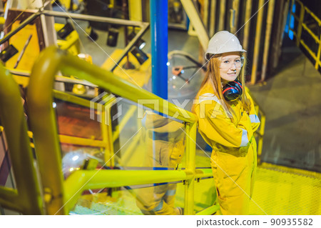 Young woman in a yellow work uniform, glasses and helmet in industrial environment,oil Platform or liquefied gas plant Young woman in a yellow work uniform, glasses and helmet in industrial environment,oil Platform or liquefied gas plant 90935582